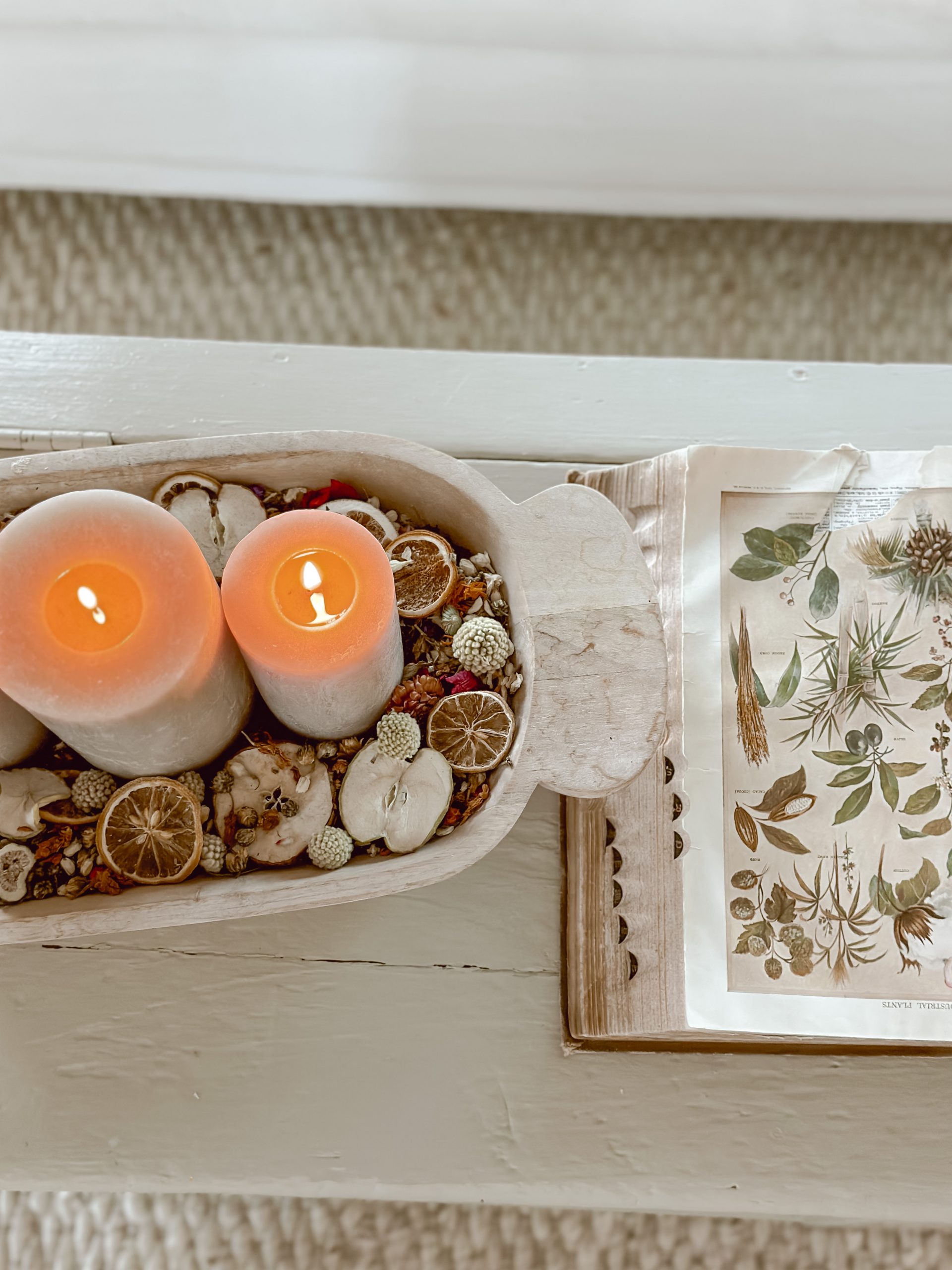 Candle with floral potpourri base in bowl along with a book on greenery 